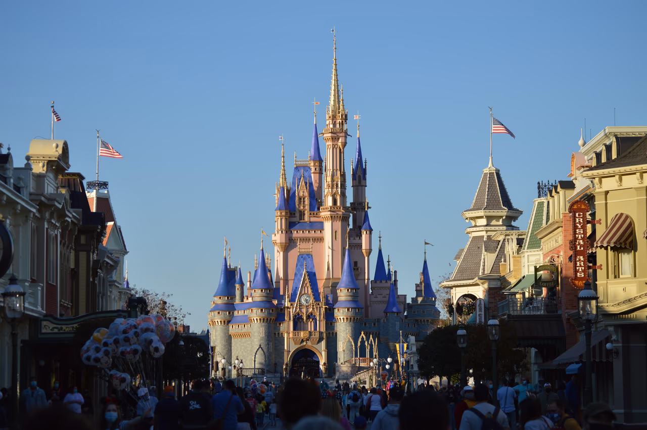 Cinderella Castle at Walt Disney World's Magic Kingdom seen down Main Street USA, with crowds and a balloon vendor in the foreground under a clear sky