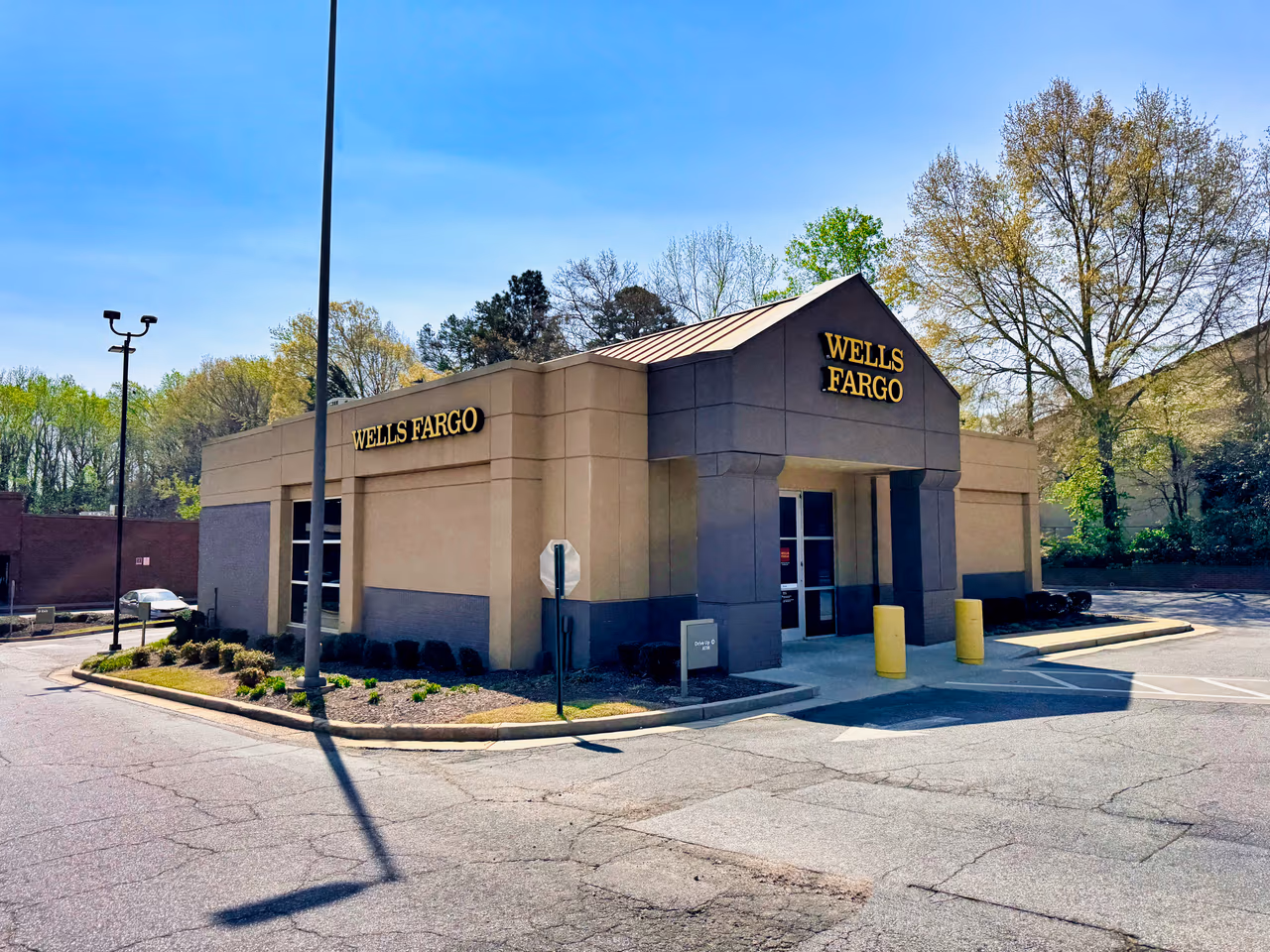 A modern single-storey bank branch in tan and brown stucco with Wells Fargo signage, photographed from the parking lot under a clear blue sky