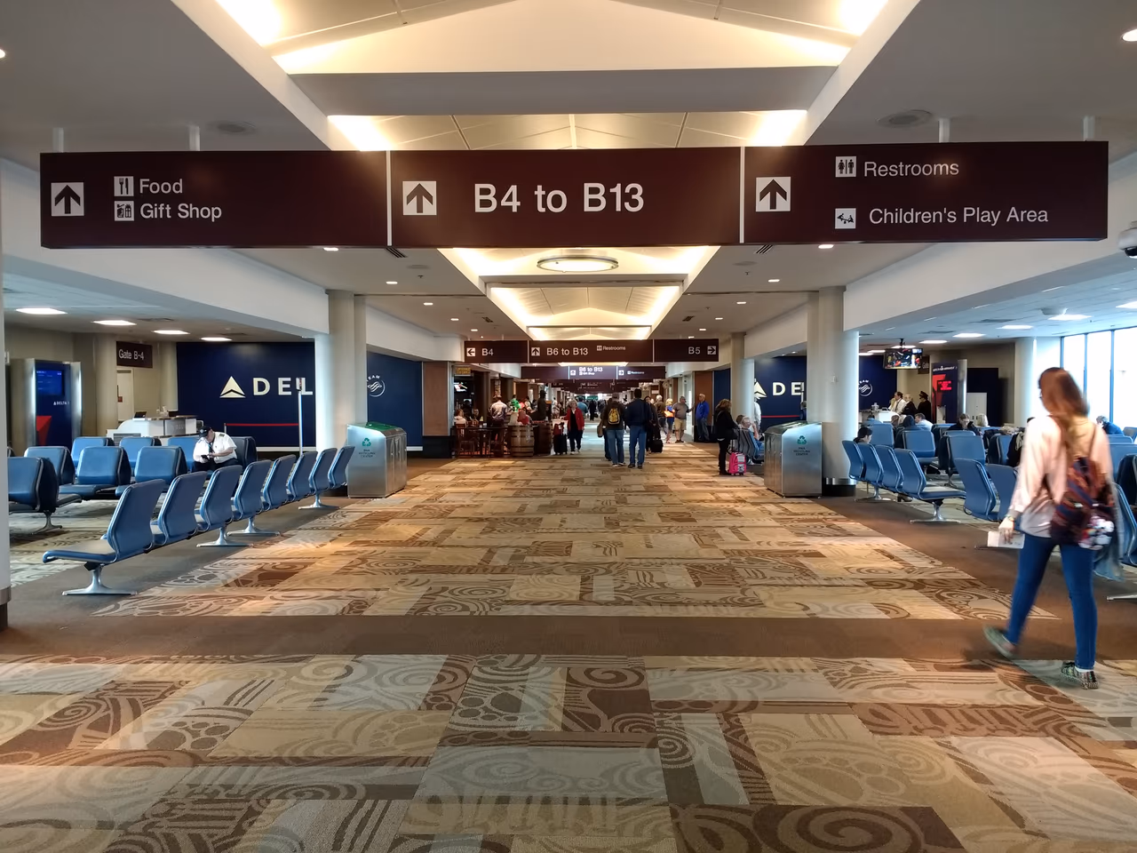 Concourse B at Nashville International Airport, with brown overhead signs reading B4 to B13, Delta gate desks along the left wall and rows of blue seating on patterned carpet