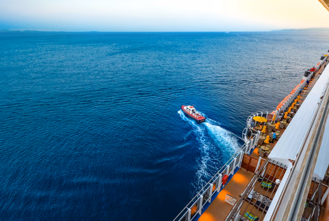 An aerial view of a large cruise ship and a small boat on the open ocean at sunset
