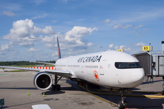 An Air Canada Boeing 777 parked at an airport gate under a clear blue sky