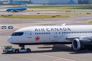 An Air Canada Boeing 787 being pushed by a tug on an airport apron, with KLM jets and a KLM hangar behind
