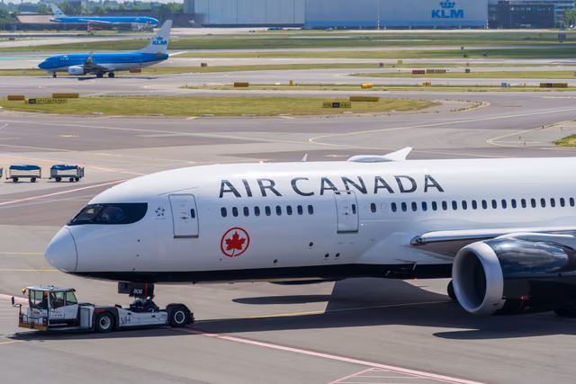 An Air Canada Boeing 787 being pushed by a tug on an airport apron, with KLM jets and a KLM hangar behind