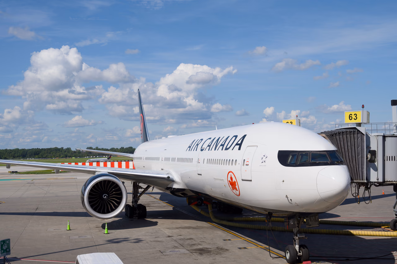 Air Canada Boeing 777 parked at an airport gate under a blue sky with white clouds