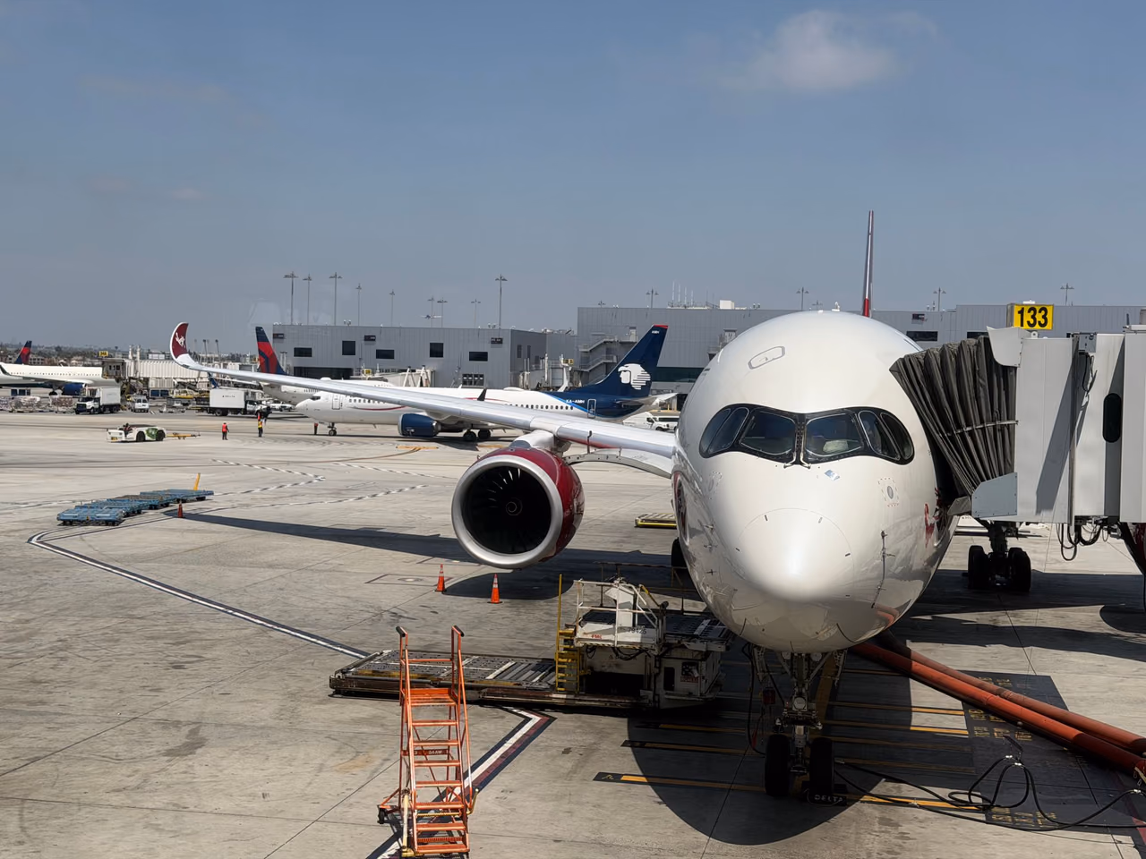 The nose of an airliner at a jet bridge gate at Los Angeles International Airport, with other airline jets parked beyond it