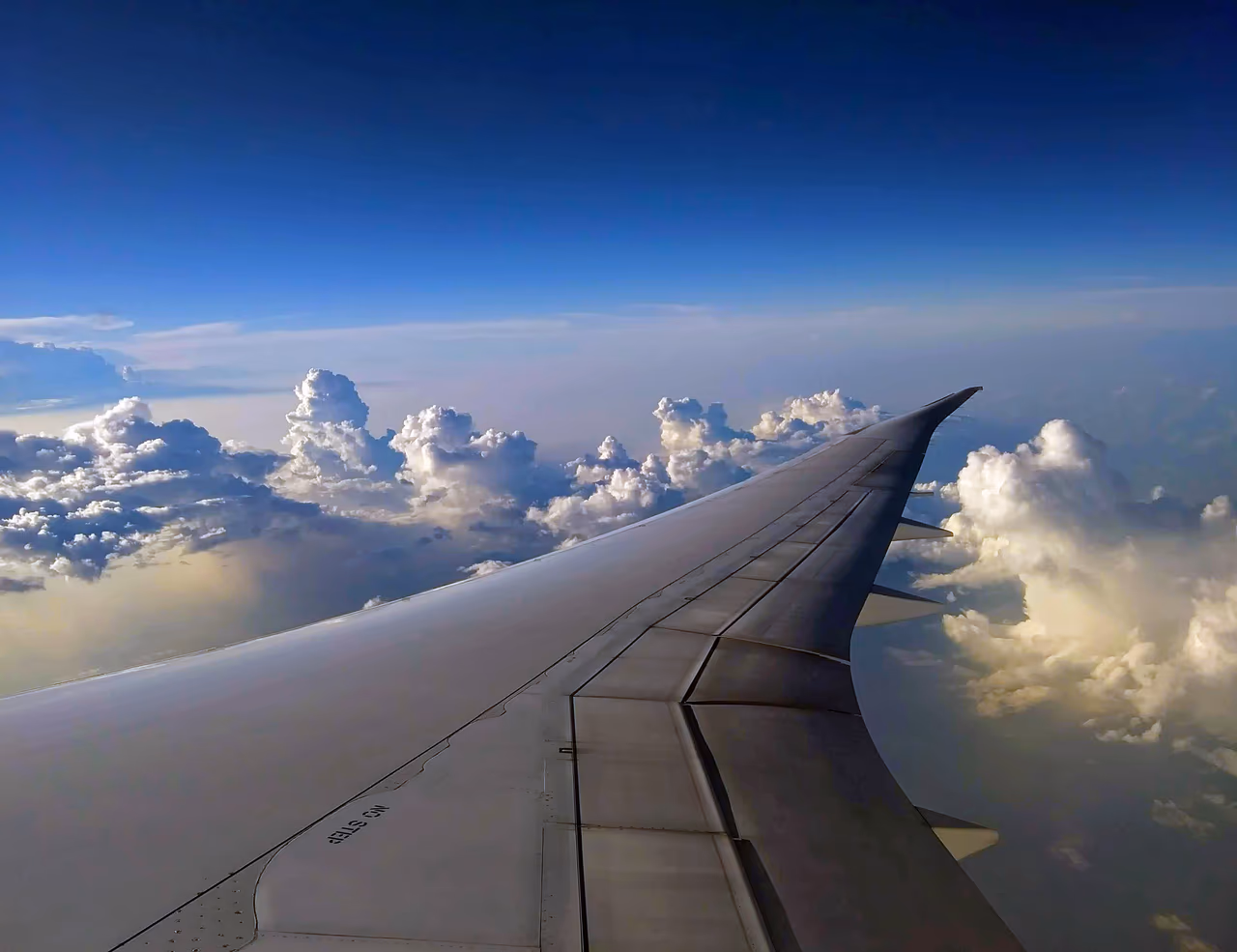 The upswept wingtip of an airliner in cruise, seen from a cabin window above a bank of cumulus cloud
