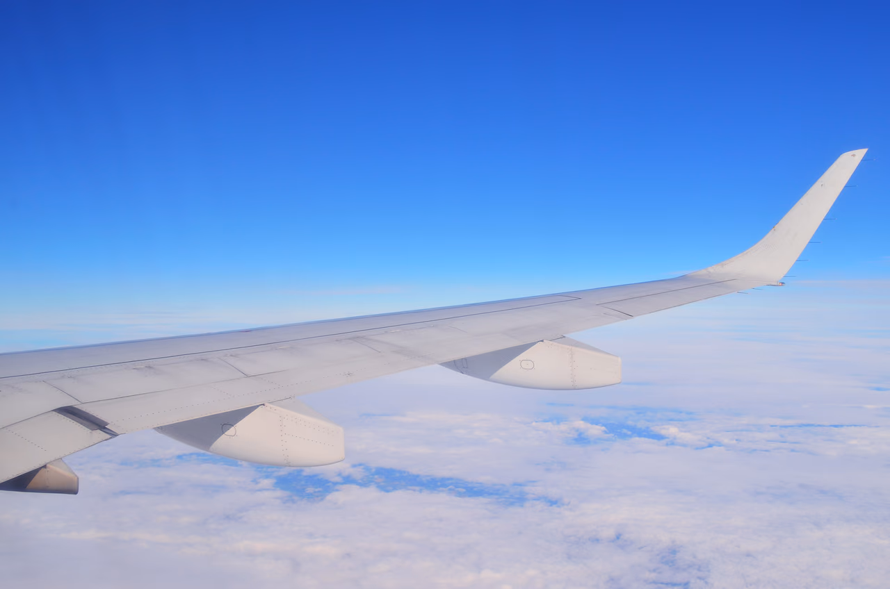 Airplane wing and upturned winglet above a layer of white clouds under a clear blue sky, seen from a cabin window