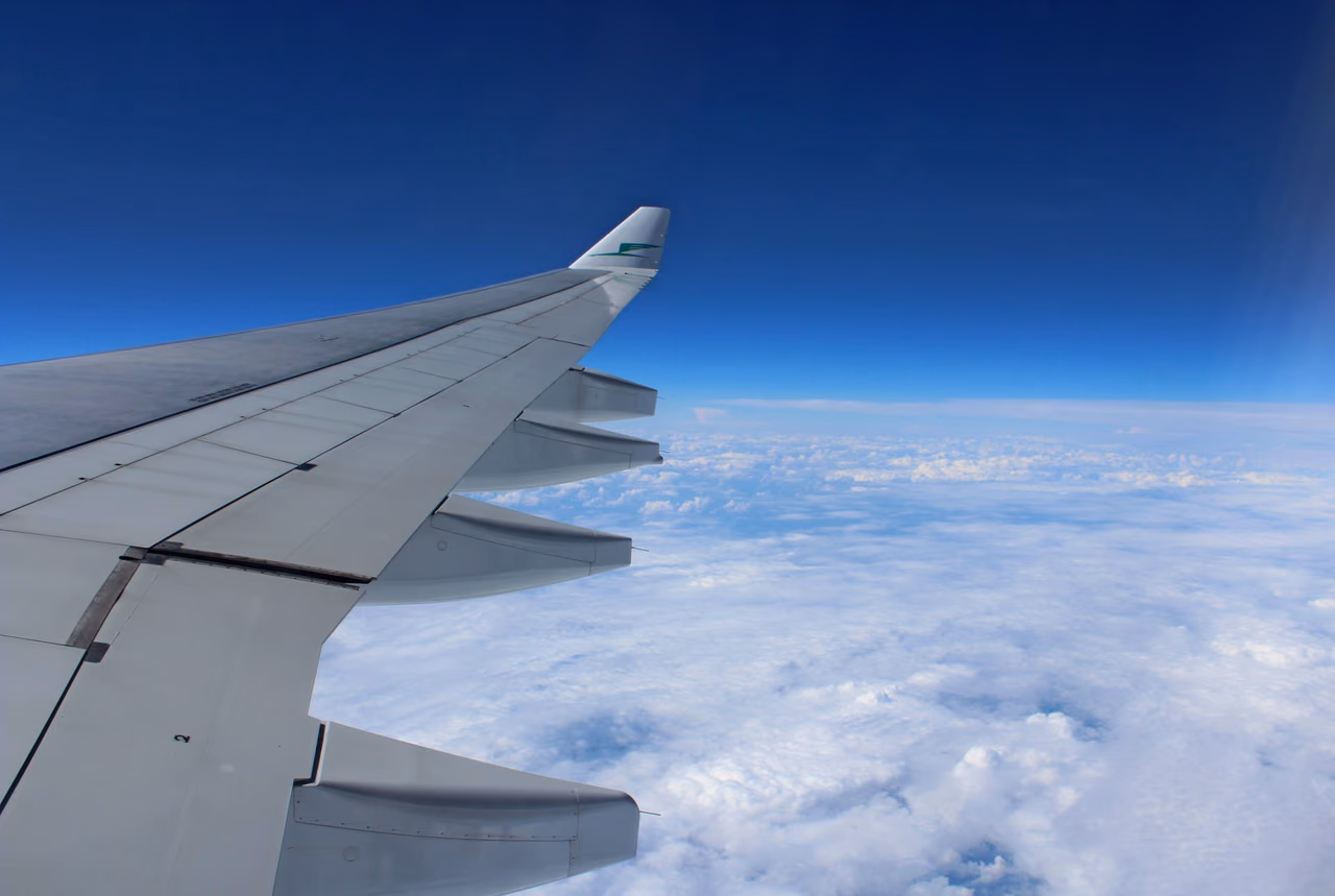 Airplane wing in flight above a layer of clouds under a blue sky