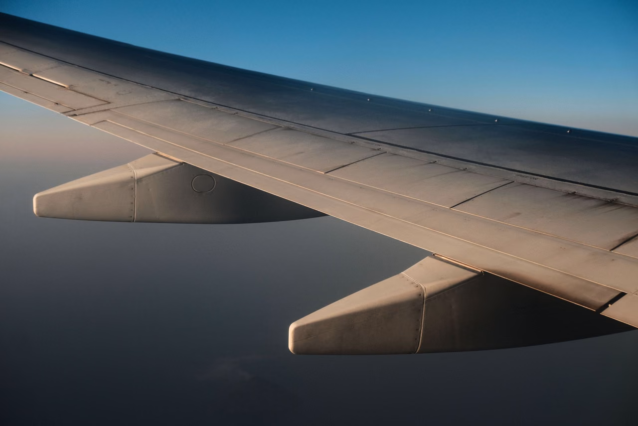 An airplane wing seen from a passenger window in flight, with flaps extended and a clear blue sky above
