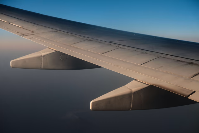 An airplane wing seen from a passenger window in flight, with flaps extended and a clear blue sky above