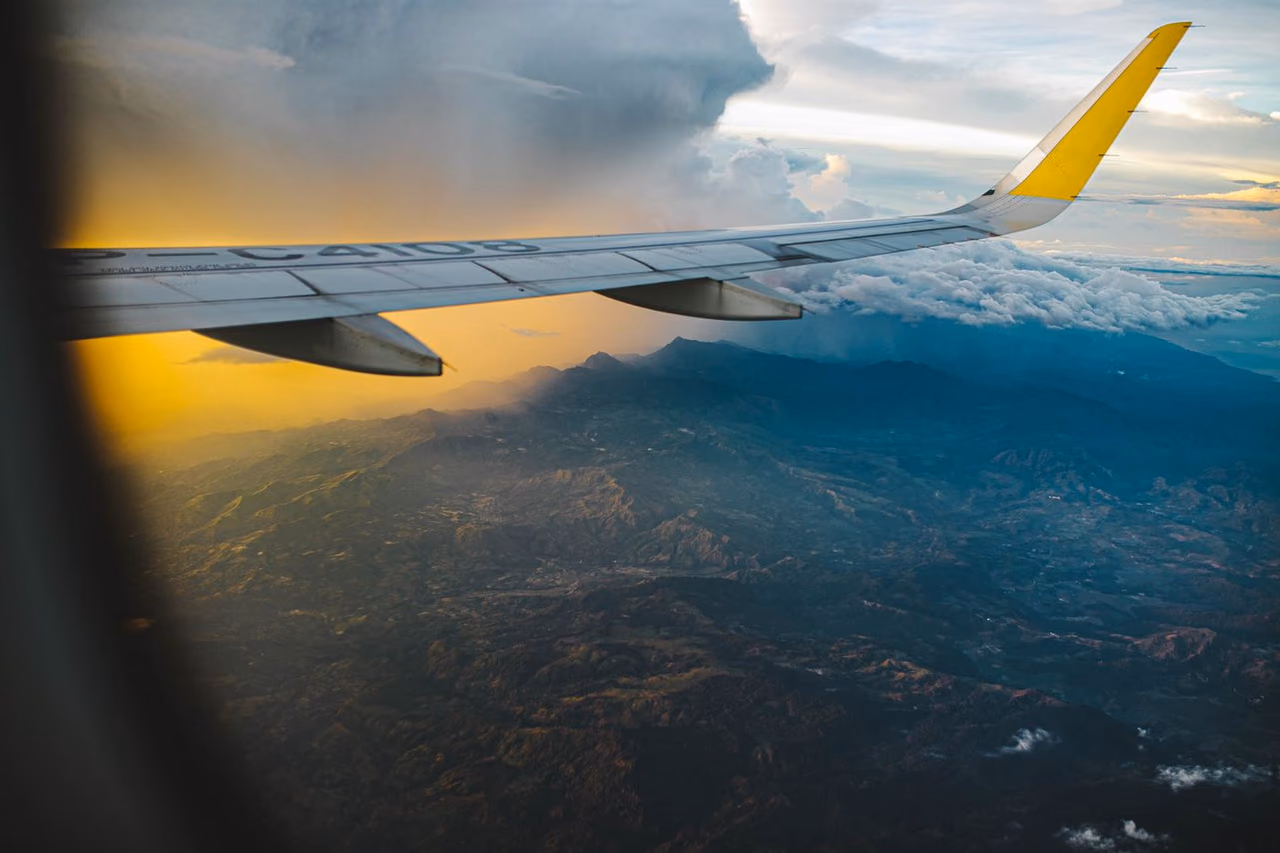 Airplane wing seen from a cabin window above dramatic clouds at sunset