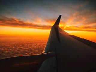 An airplane wing against a vivid red and orange sunset sky, with clouds below