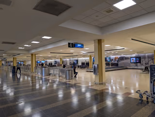 An airport baggage claim hall with an empty carousel, a sign reading 4 above it and a few travelers waiting near the belt