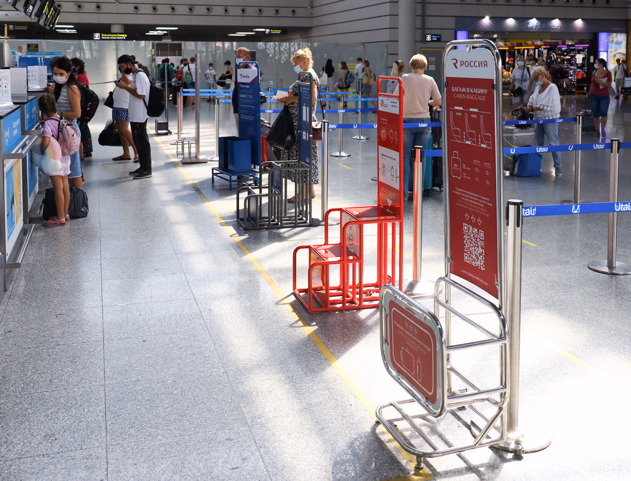 Metal carry-on bag sizer frames standing in an airport check-in hall beside queue barriers and a cabin baggage information sign