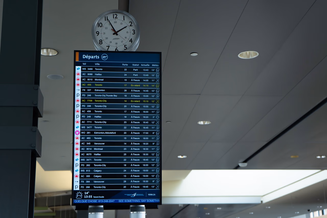 A French-language departures screen at Ottawa's airport under a wall clock, with two Air Canada flights to Toronto marked delayed in yellow