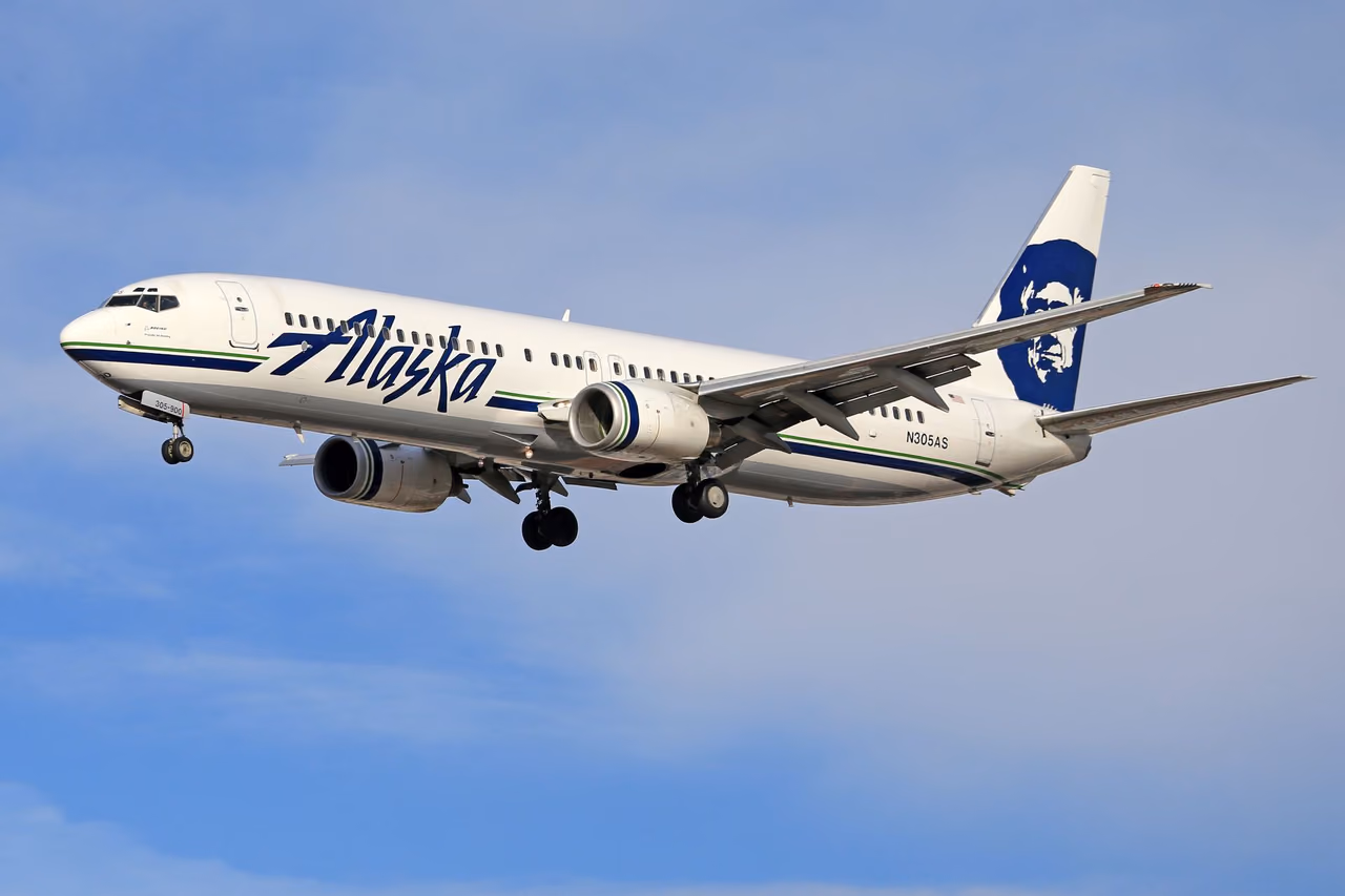 An Alaska Airlines Boeing jet in flight against a clear blue sky