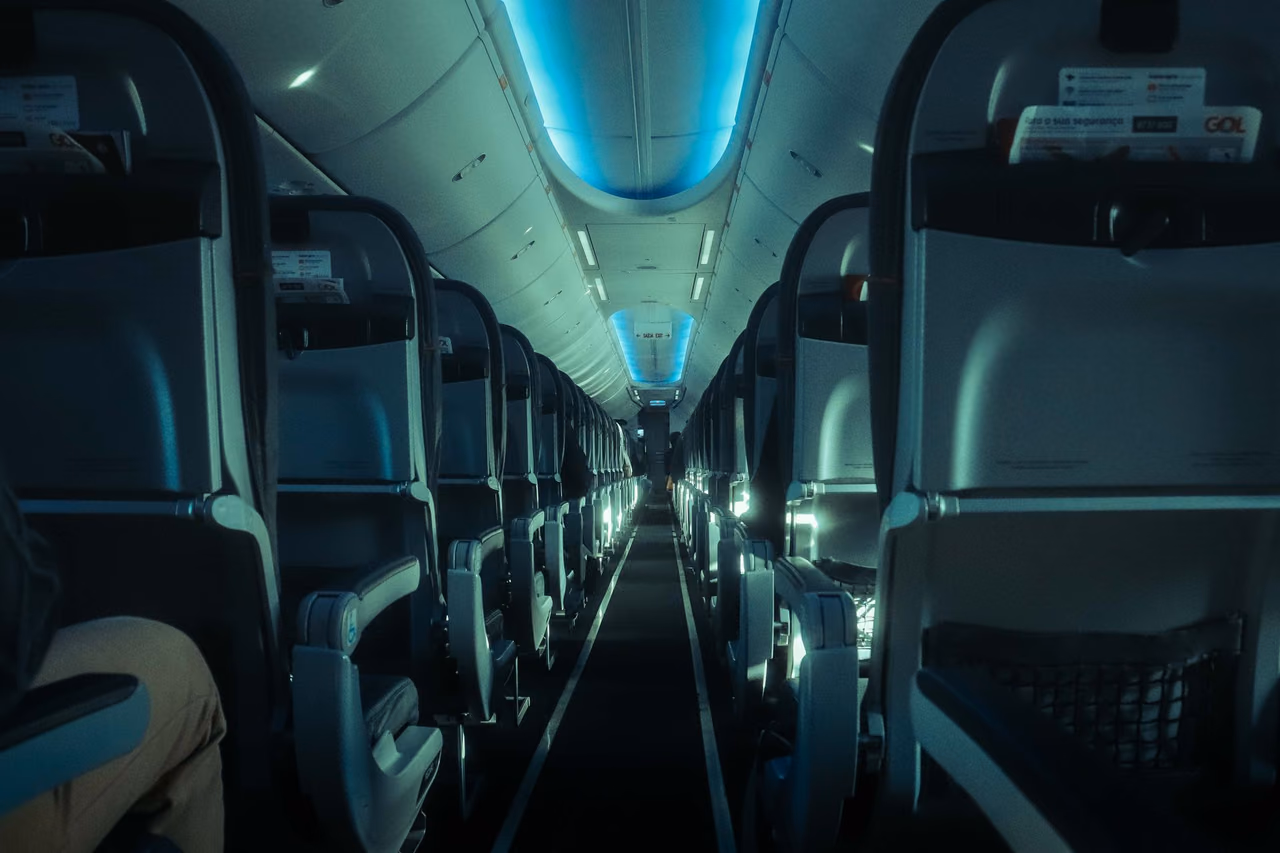 Aircraft cabin aisle with rows of seats on both sides under blue ambient lighting