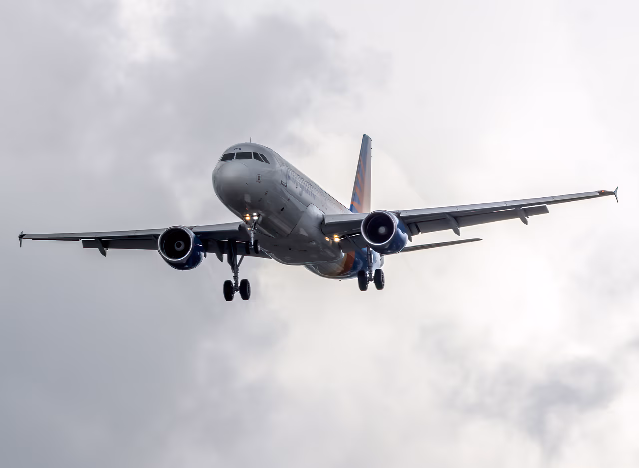 An Allegiant Air Airbus A320 on final approach with its landing gear down, against a bank of grey cloud