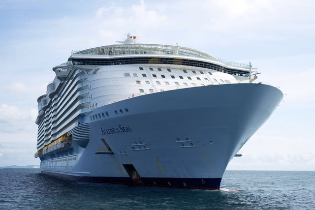 The bow of Royal Caribbean's Allure of the Seas, an Oasis-class ship, seen from the water against a pale sky