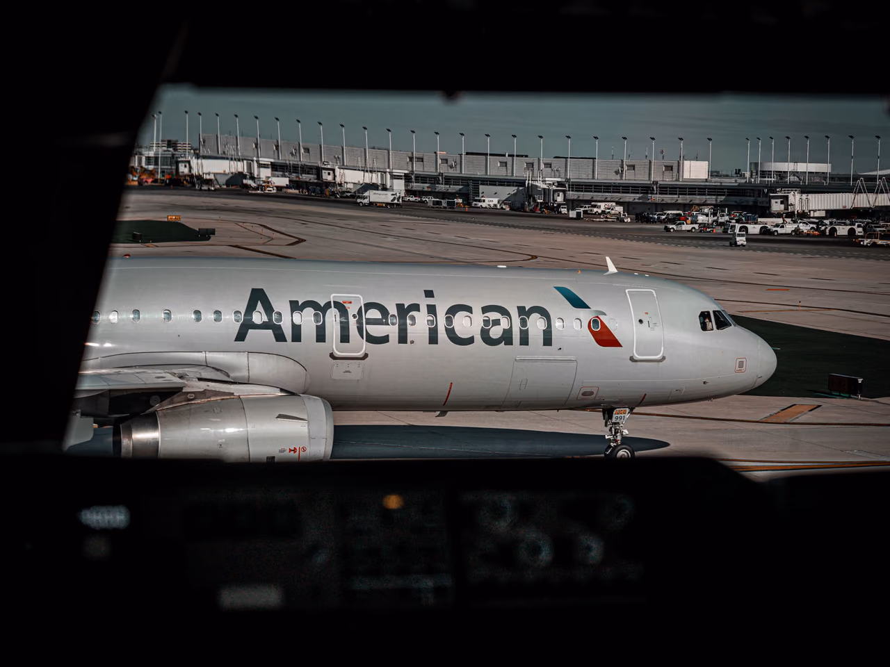 An American Airlines jet taxiing past a terminal, seen through a cockpit window