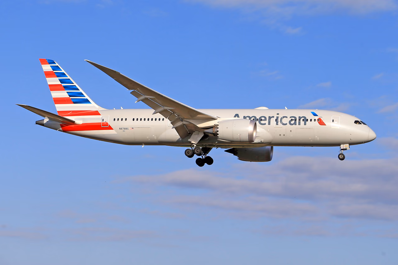An American Airlines Boeing 787 Dreamliner with its landing gear down against a blue sky