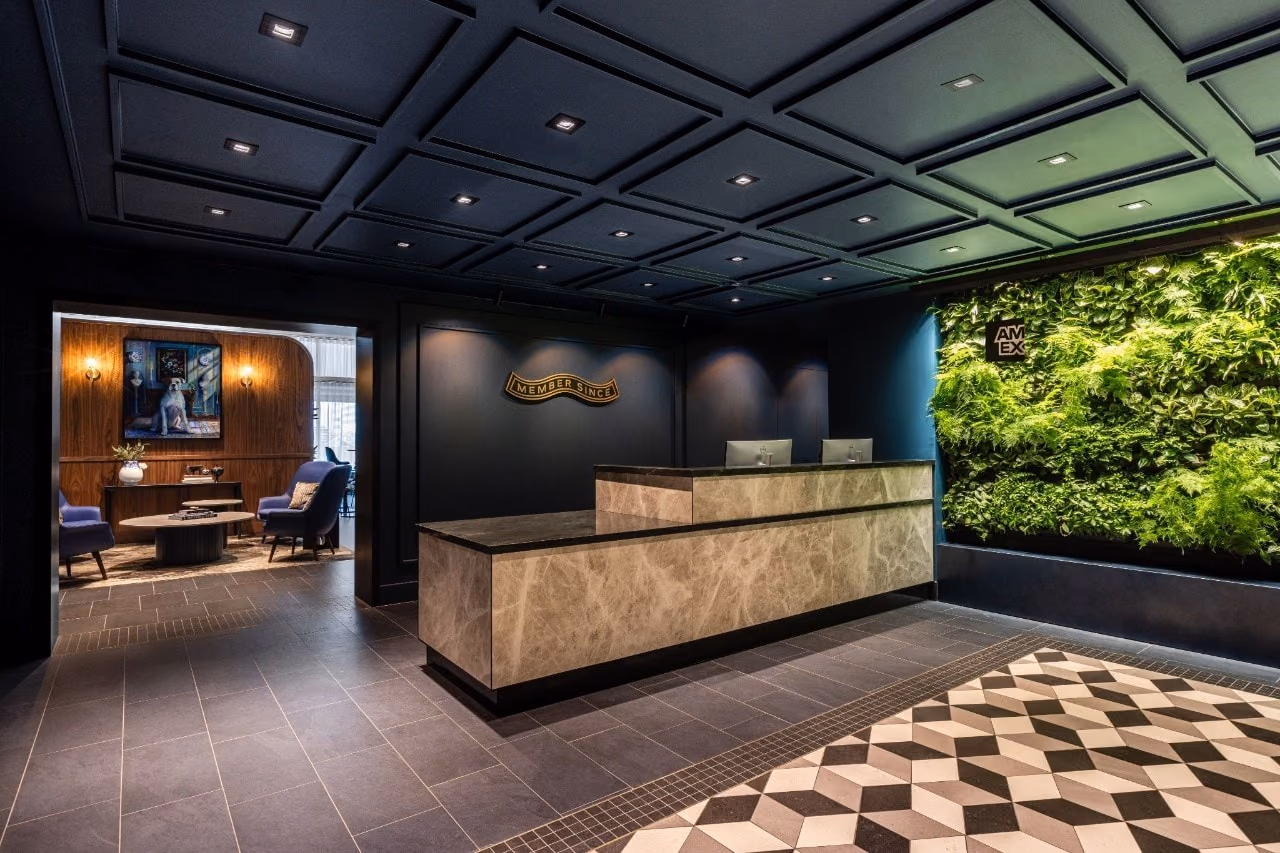 Reception desk at the Amsterdam Schiphol Centurion Lounge, with a marble counter and a plant wall bearing the Amex logo