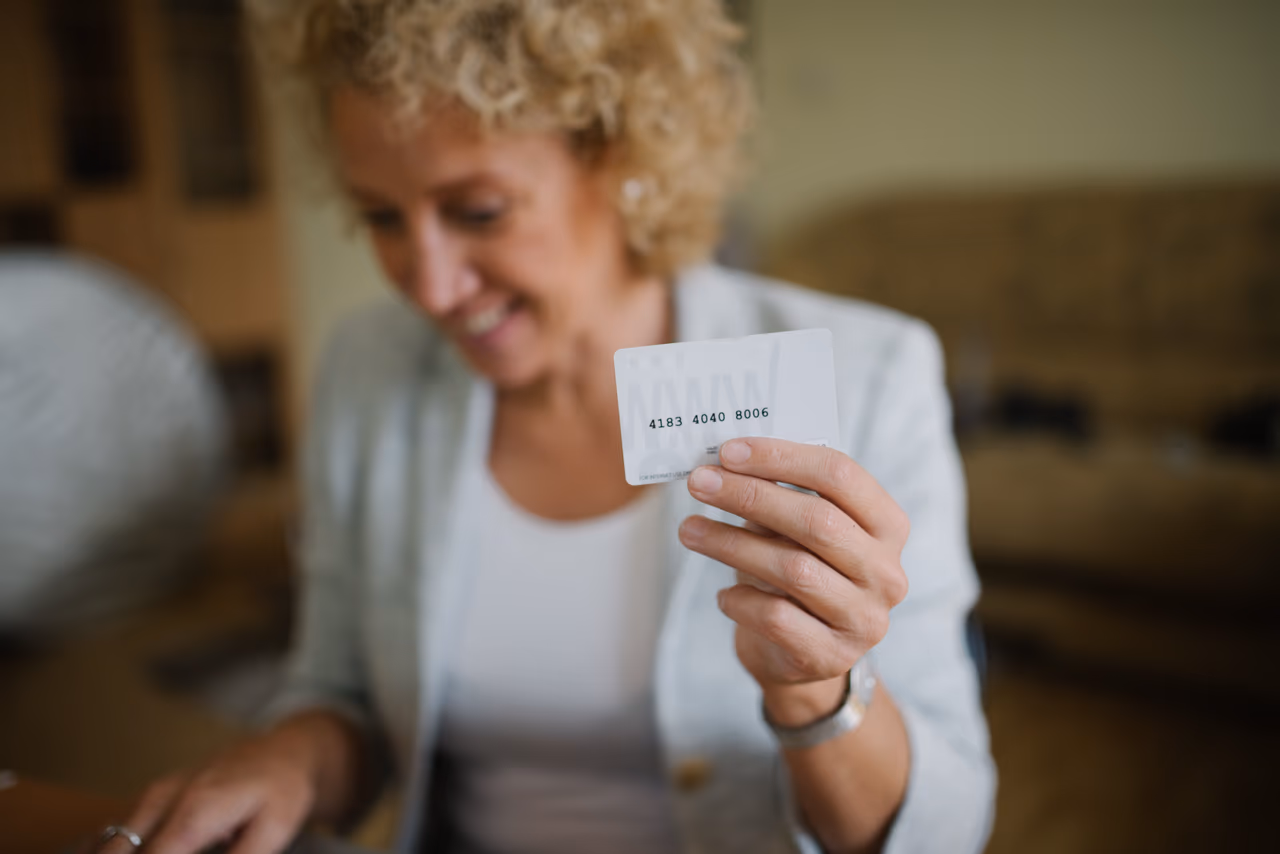 A woman holding an unbranded white payment card out towards the camera in a softly lit living room