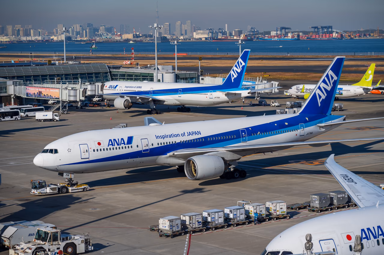 ANA Boeing 777 in the blue-and-white Inspiration of Japan livery being pushed back at Tokyo Haneda, with Tokyo Bay and the city skyline behind