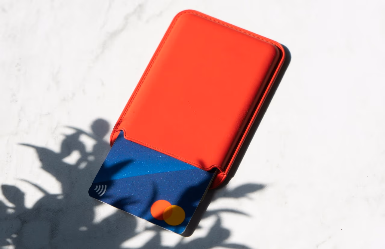 Blue credit card sliding out of a red card wallet on a white marble surface