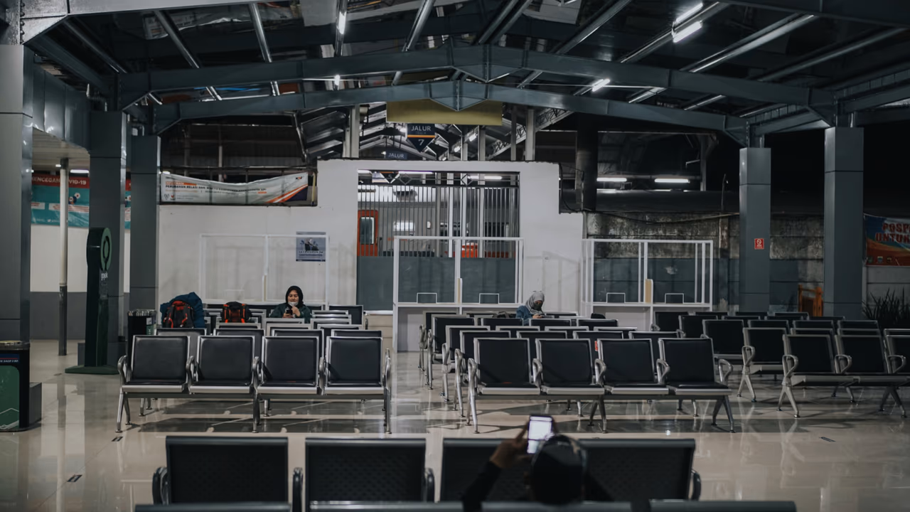 Empty train station waiting area with rows of seats and a few passengers.