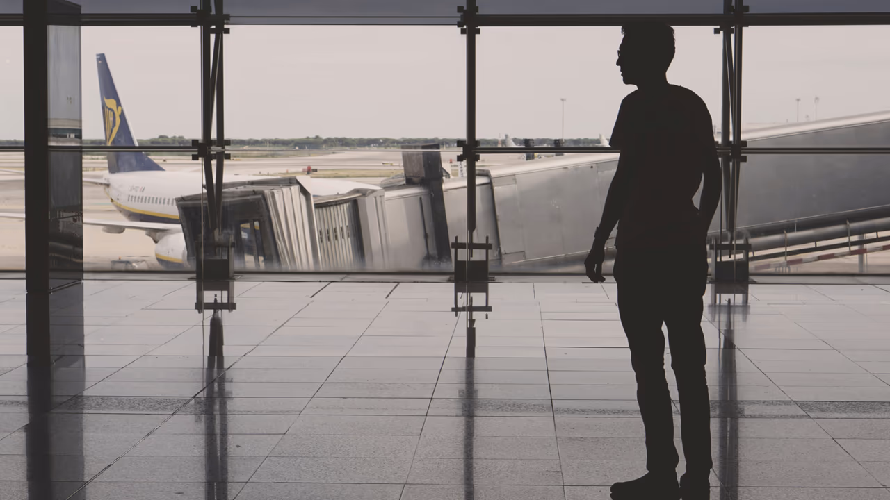Traveler at airport gate looking at plane through terminal window