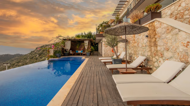 Infinity pool with lounge chairs at luxury hillside resort at sunset