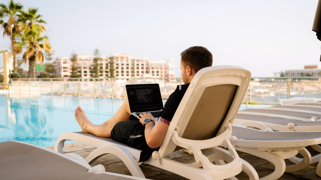 Business traveler working on laptop at luxury hotel pool overlooking resort property