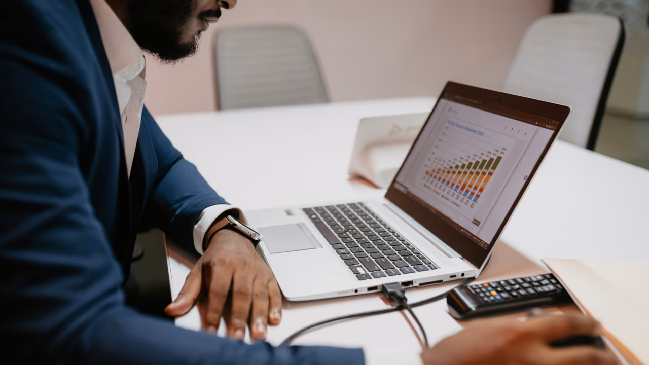 Businessman reviewing charts on laptop with calculator on desk.