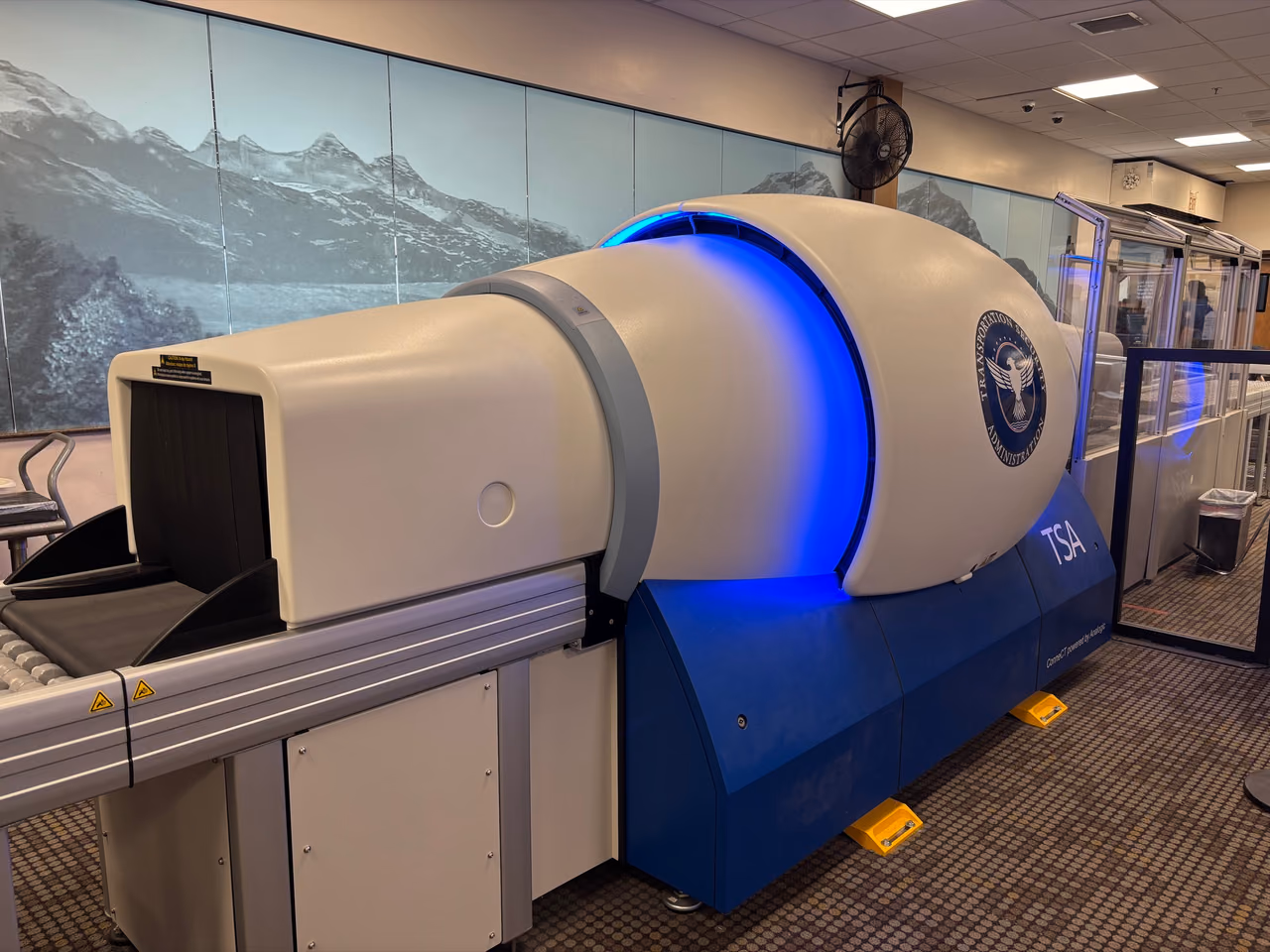 A TSA computed tomography carry-on scanner with a glowing blue ring and the TSA seal at the Juneau airport checkpoint