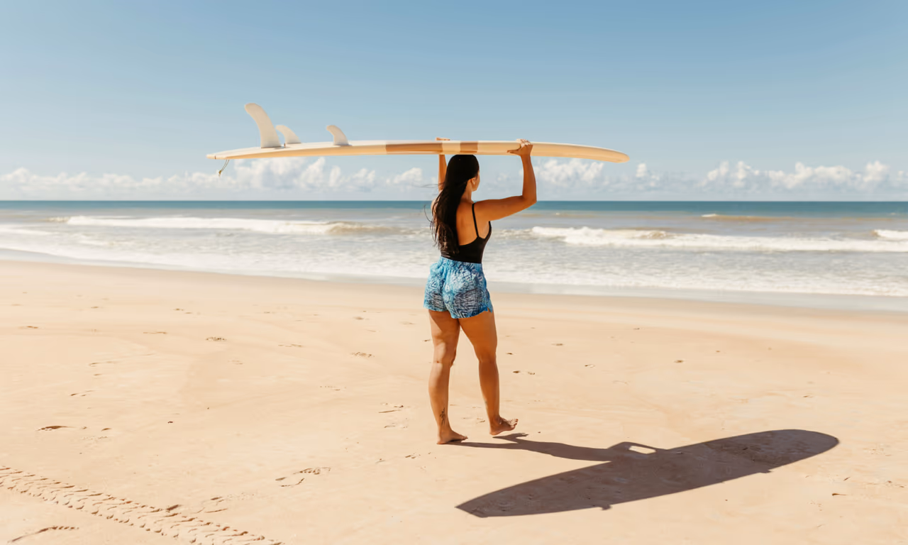 girl on the beach balancing a surfboard on her head thinking about her next quest in the ocean