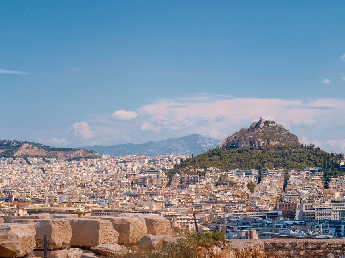 Athens rooftops spreading toward Mount Lycabettus, seen from the ancient stone blocks of the Acropolis
