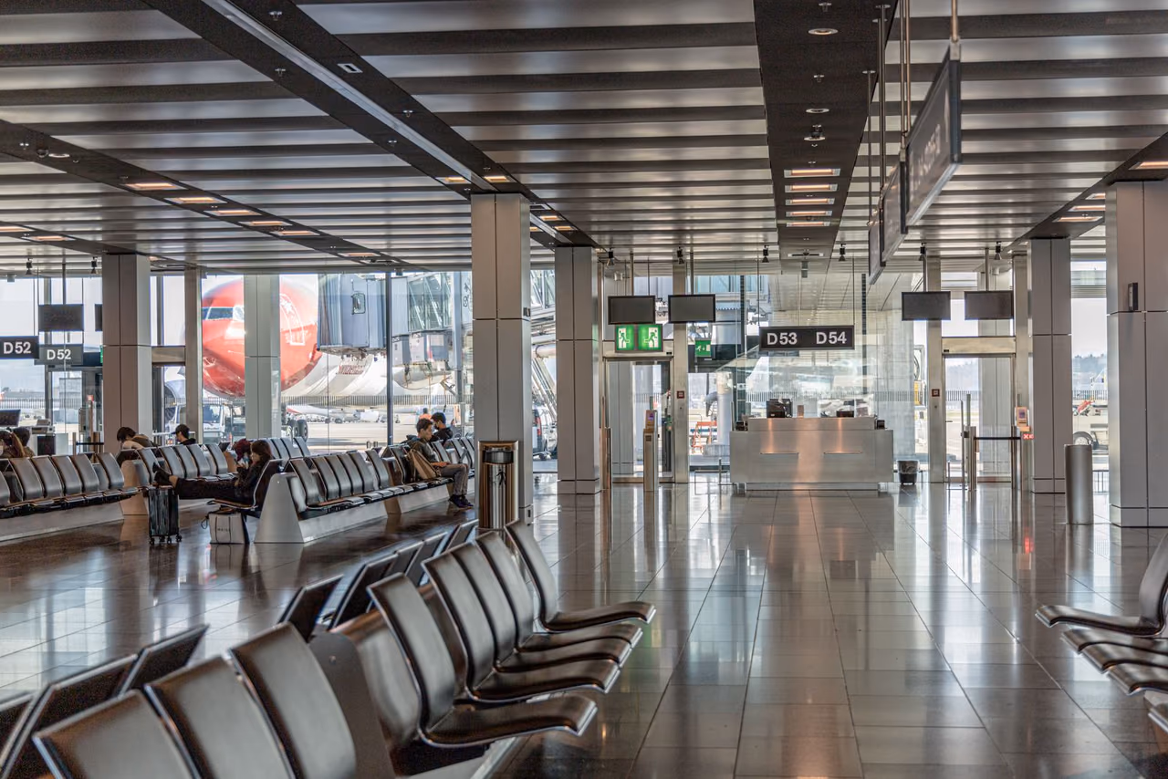 Bright airport terminal with rows of seats and a parked airliner visible through floor-to-ceiling windows