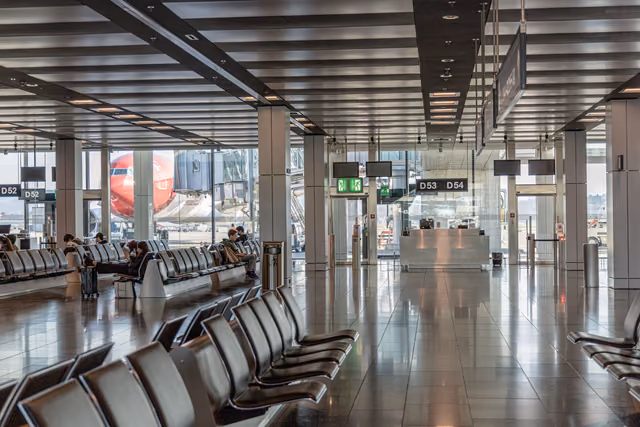 Bright airport terminal with rows of seats and a parked airliner visible through floor-to-ceiling windows