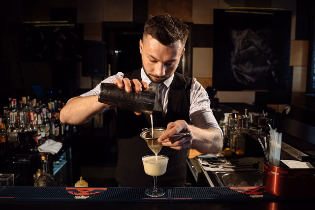Bartender pouring a cocktail through a strainer at a bar