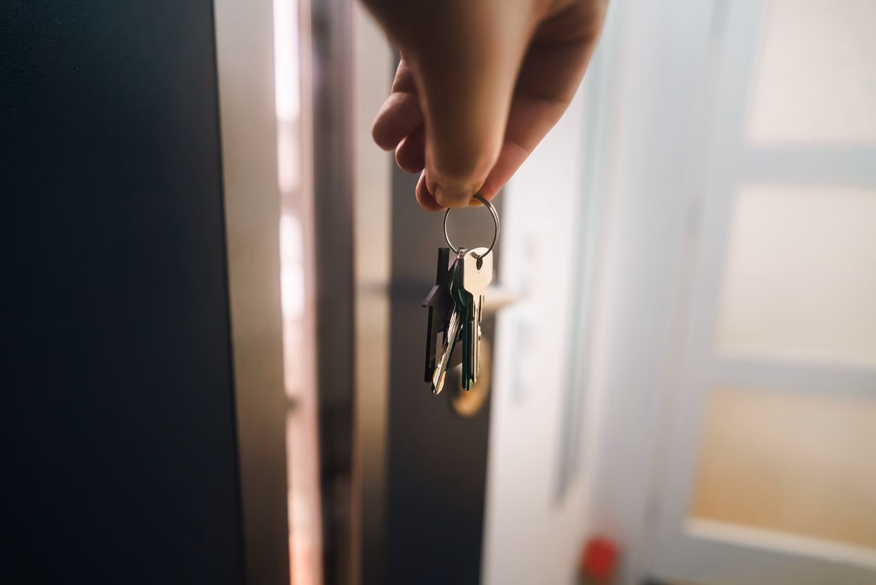 A hand holding a set of keys with a house-shaped fob next to an open door