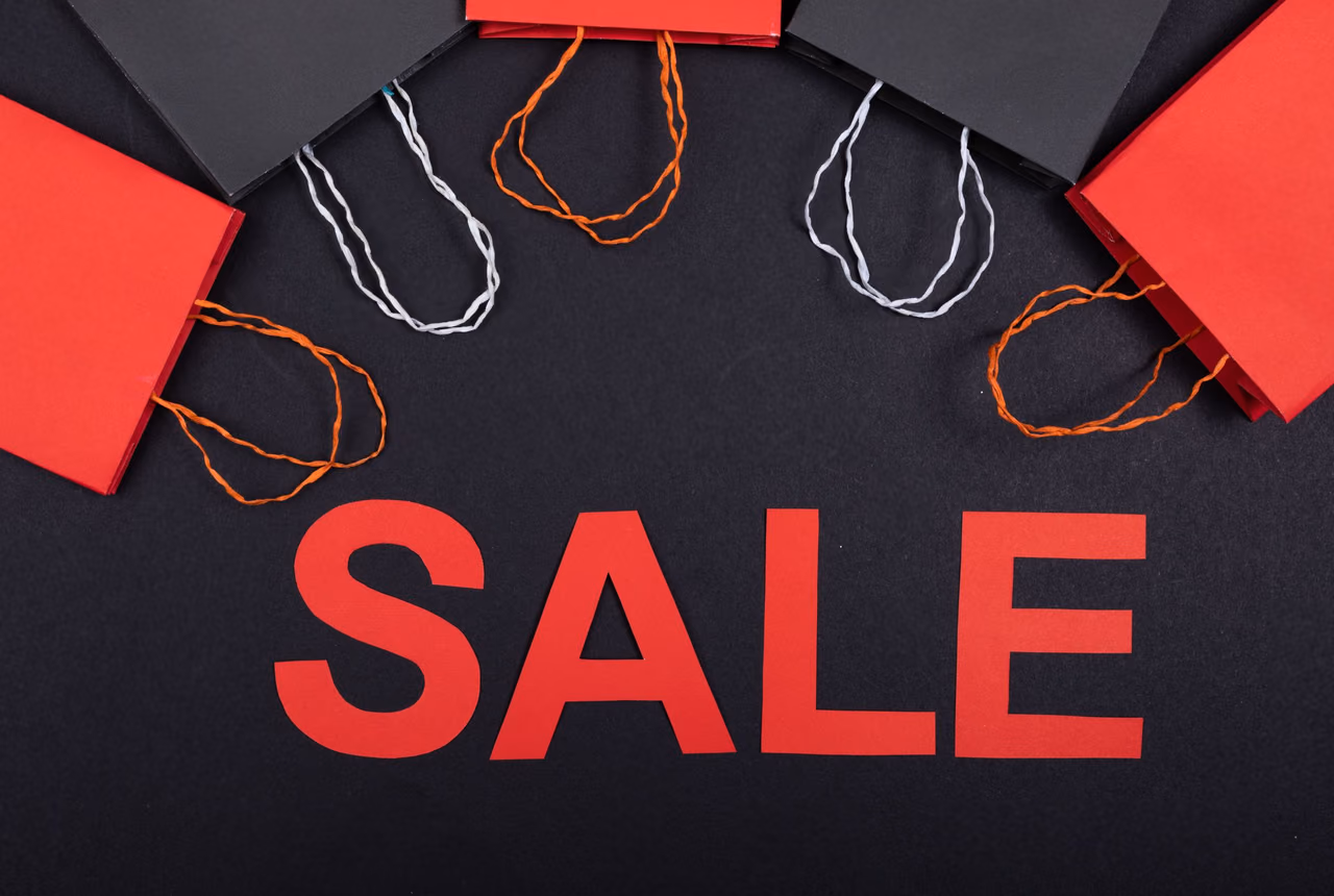 Red and black paper shopping bags arranged above the word SALE cut from red paper on a black background