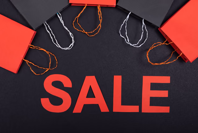 Red and black paper shopping bags arranged above the word SALE cut from red paper on a black background