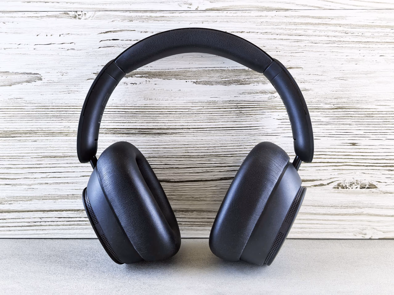 A pair of black over-ear wireless headphones standing upright against a whitewashed wooden wall