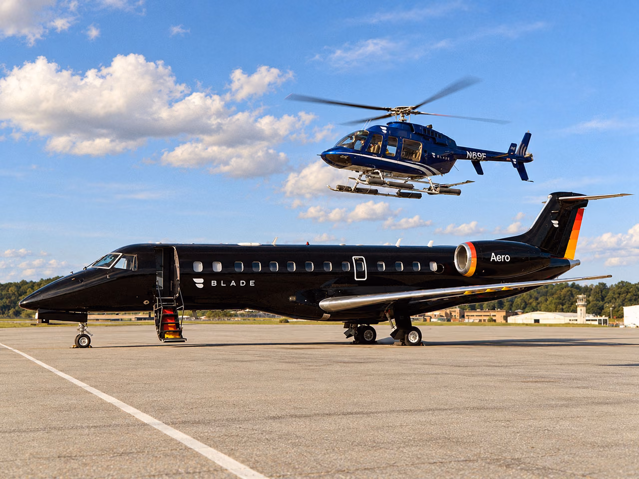 A black jet with Blade and Aero markings parked on an airport apron with its stairs down, as a dark blue helicopter flies overhead