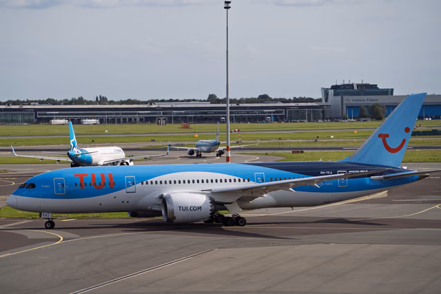 A Boeing 787 Dreamliner in blue and white livery taxiing past the terminal at Amsterdam Schiphol Airport