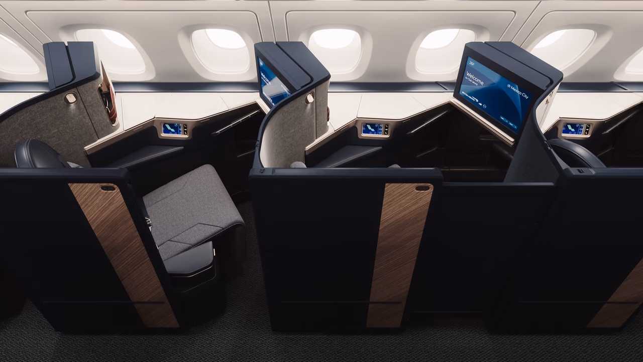 Three navy British Airways Club Suites with walnut-effect panels by the cabin windows, one screen showing a welcome message