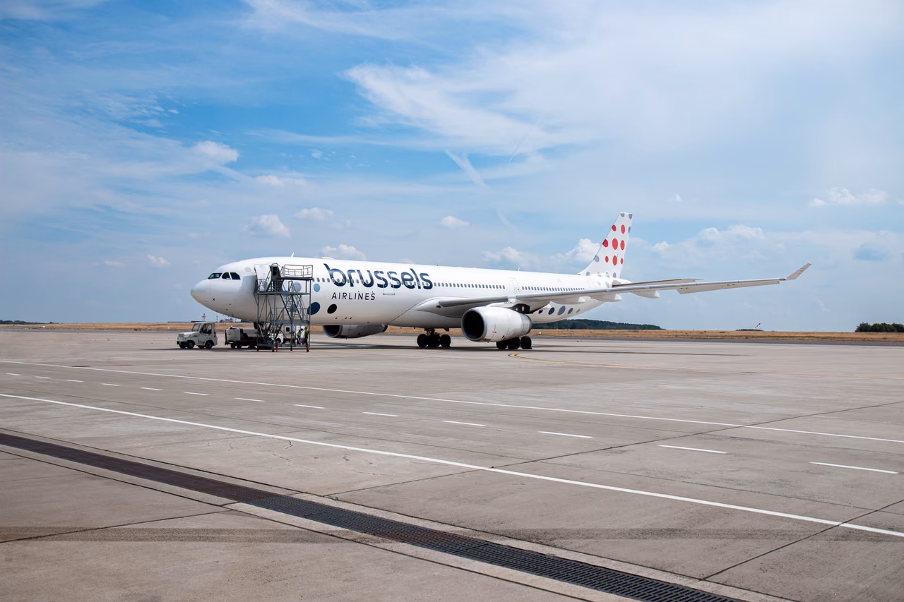 A Brussels Airlines Airbus A330 parked on an open apron with boarding stairs at the front door under a blue sky