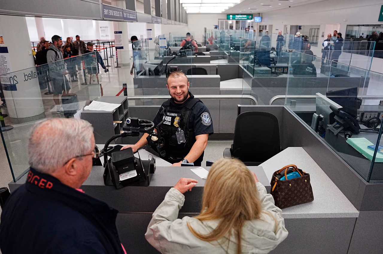 A smiling CBP officer at an inspection booth at Baltimore/Washington International Airport, facing two travelers