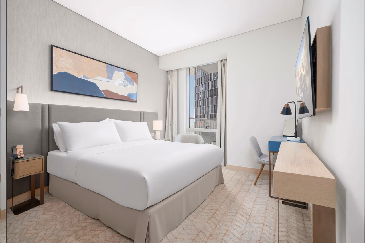 Modern hotel room with a king bed, framed artwork and a window looking out over the city